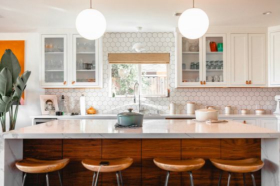 A sunlit family kitchen with a wooden island, pale cabinets and plants on the counter.